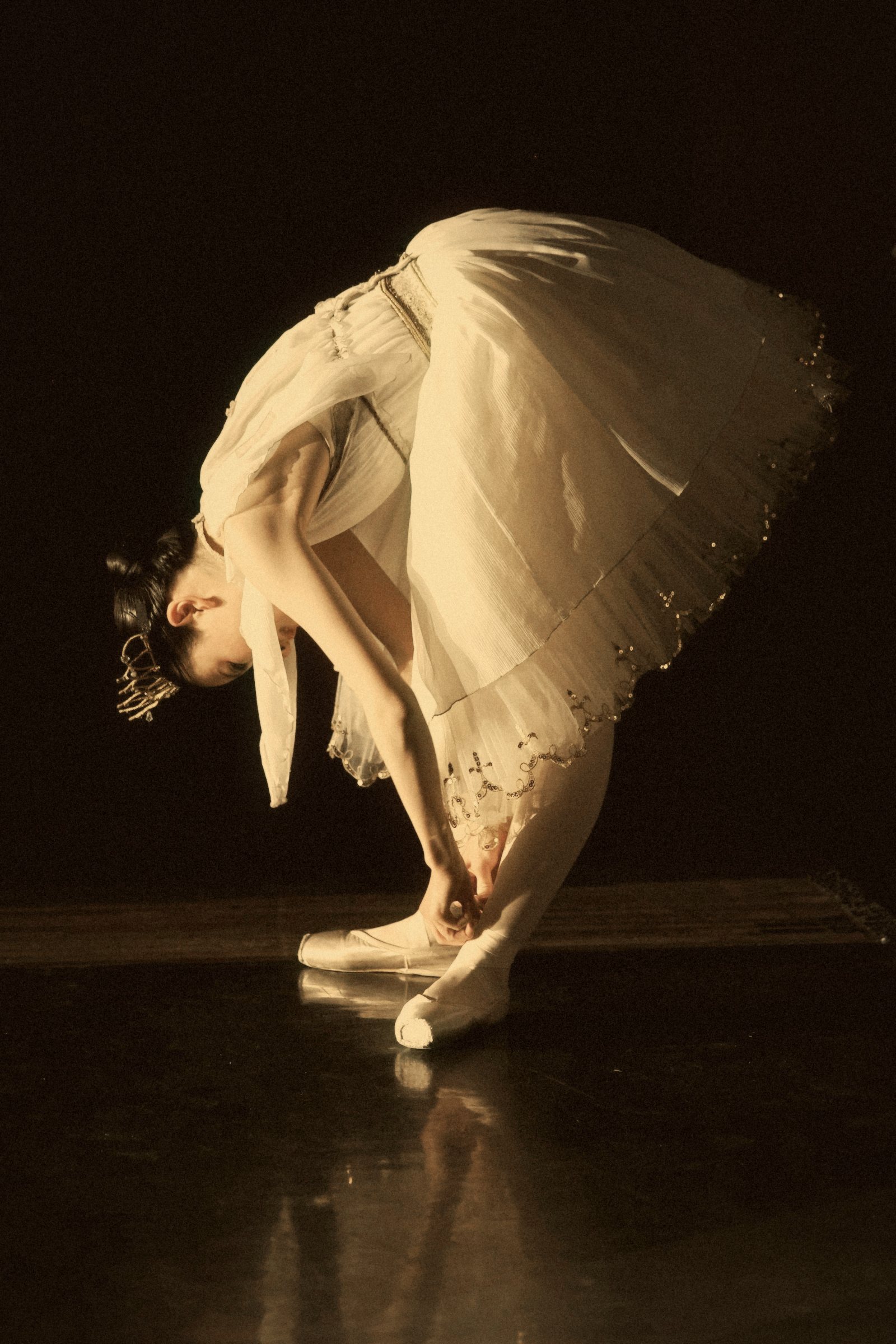 Bailarina con tutú inclinada en la penumbra para atarse la punta
