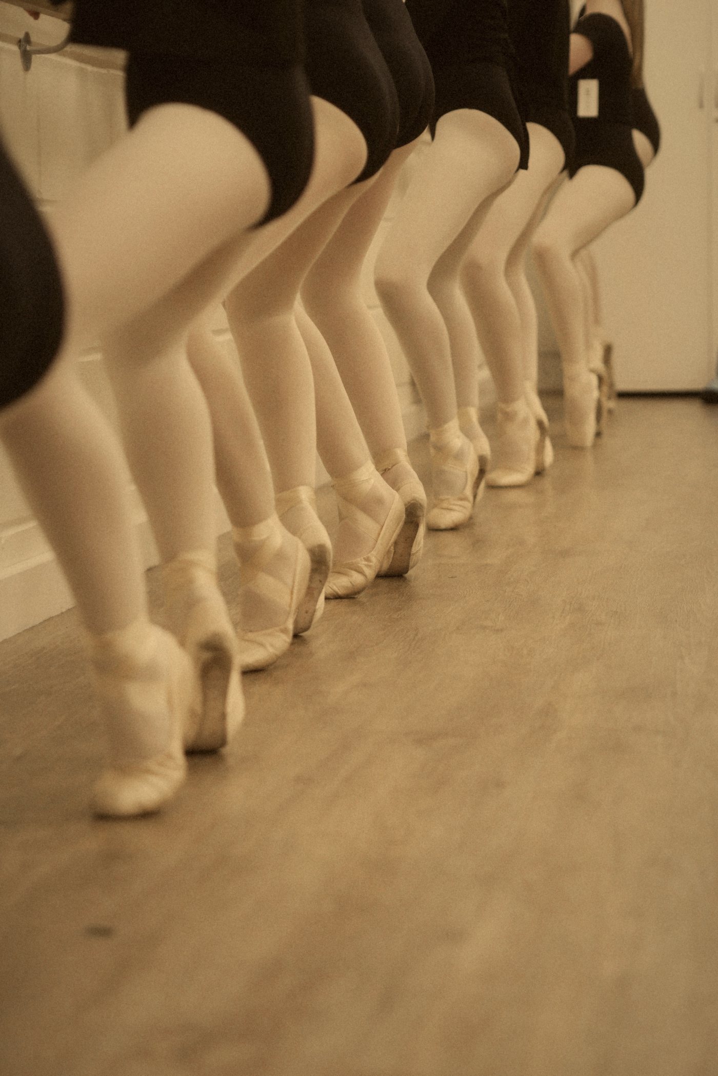 Fila de piernas con medias rosas y puntas de ballet sobre un suelo de madera